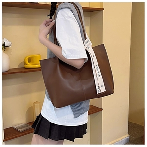 Side view of a large dark brown tote bag with decorative fashion letter ribbon on a model