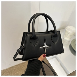 Detail of a black trapezoid crossbody bag featuring a silver metal star ornament
