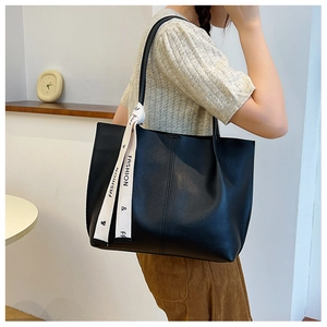 Detail of a large black faux leather tote bag featuring a decorative fashion ribbon