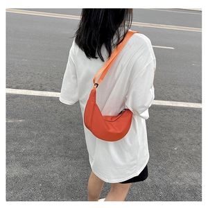 Dettaglio di una borsa a tracolla a mezzaluna arancione vivace indossata con t-shirt bianca