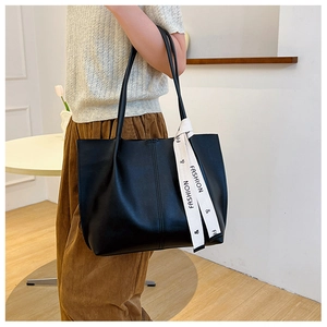 Detail of a large black faux leather tote bag featuring a decorative fashion ribbon on the handle