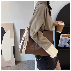 Close-up of brown faux leather tote bag with stylish white fashion logo strap detail