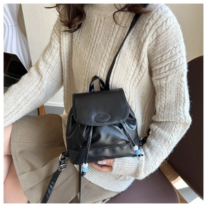 Détail d'un mini sac à dos noir avec cordon et perles bleues porté sur un pull beige