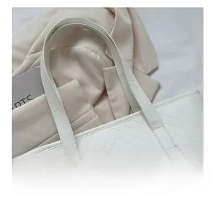 Detailed close-up of V-shaped stitching texture and slim handles on a white tote bag