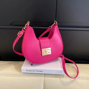 Rose pink saddle shoulder bag with gold buckle and adjustable strap on white books