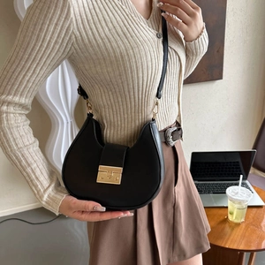 Minimalist black leather hobo saddle bag with gold buckle shown in a warm lifestyle setting