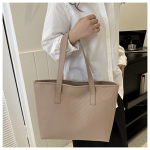 Close-up of beige tote bag with V-shaped quilted stitching and dual slim shoulder straps