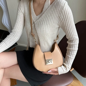 Minimalist beige crescent saddle bag with metal buckle shown on a model in a warm setting