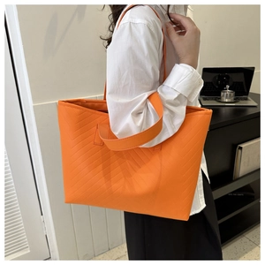 Orange quilted faux leather tote bag being carried by a model in an office setting