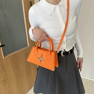 Orange crossbody handbag with silver star detail paired with a white knit top
