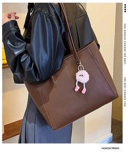 Brown leather tote bag featuring a decorative pink fur ball charm and side stitching