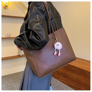 Side view of dark brown leather tote bag with a pink plush monster charm on model
