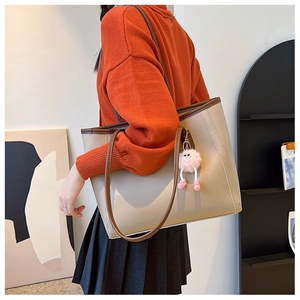 Detail of beige tote bag with brown trim and cute pink plush ball charm on strap