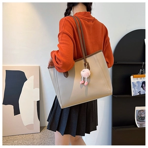 On-shoulder view of large beige tote bag with brown straps and plush charms