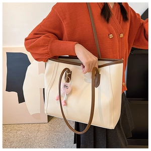 Detail of a large cream tote bag with brown trim and a cute pink plush charm accessory