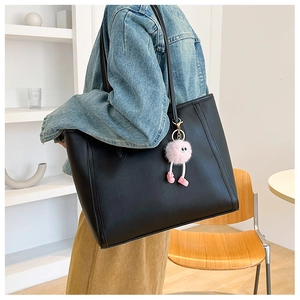 Close-up of black leather tote bag featuring a cute pink plush monster bag charm
