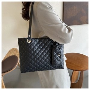 Detailed side view of black quilted tote bag set with matching mini pouch and gold hardware