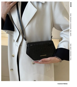 Detail shot of black faux leather crossbody bag with embossed crocodile texture and gold text