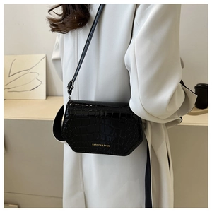 Detail of black patent faux crocodile leather bag with gold FASHION & BAGS logo on a model