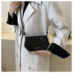 Detail of a black faux crocodile leather crossbody bag with gold fashion lettering