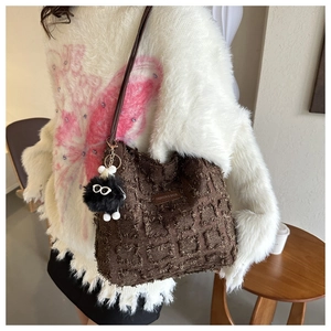 Détail du sac seau en tissu marron foncé avec charme en peluche et longue bandoulière
