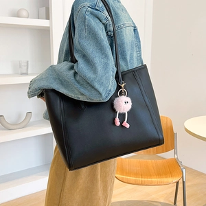Minimalist black leather tote bag with pink plush charm on a model in a modern interior