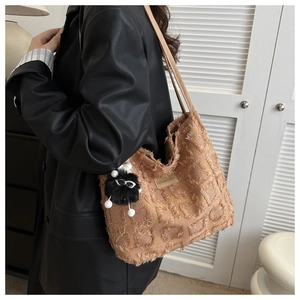 Détail d'un sac cabas marron tissé avec bords frangés et breloque en peluche sur l'anse