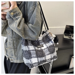 Détail d'un sac cabas à carreaux avec bords frangés, patch et pompon décoratif