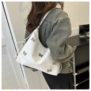Détail de sac en cuir PU blanc avec breloques papillon en argent porté à l'épaule
