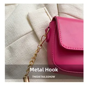Detail of golden metal hook and chain links on a magenta leather crossbody bag