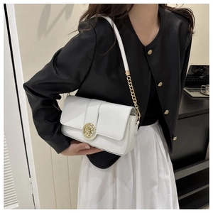 White leather shoulder bag with ornate gold buckle worn by model in chic outfit