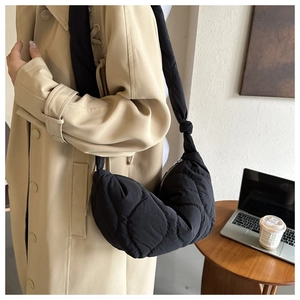 Detail of black quilted crescent bag with knotted strap on a desk with laptop