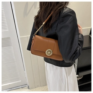 Detail of a brown leather shoulder bag with a gold buckle and chain strap on a model
