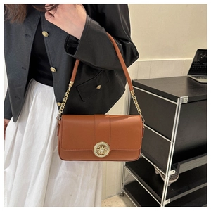 Detail of a brown leather shoulder bag with a gold hollowed-out buckle and chain strap