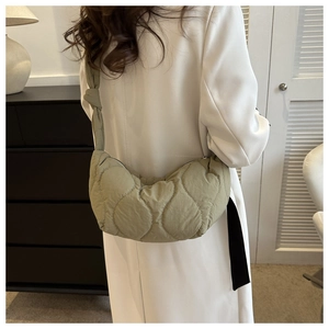 Detail of light olive puffer tote bag with quilted wavy pattern and knotted strap on model