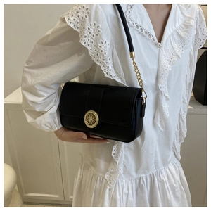 Detail of a black leather crossbody bag featuring a signature round gold buckle closure
