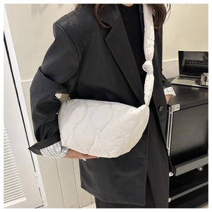 Detail of white quilted cloud tote bag with wide strap and knot decoration on black blazer
