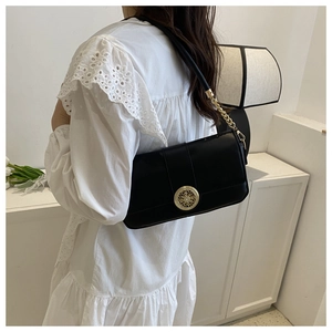 Close-up of black leather bag featuring a gold floral buckle and metal chain strap
