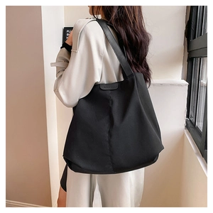 Detail of minimalist black oversized tote bag showing wide strap and textured nylon fabric