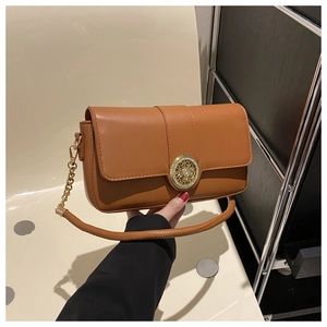 Detail of tan leather crossbody bag featuring a large circular gold rhinestone buckle