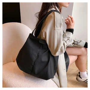 Large black canvas tote bag with leather straps worn by model in a cozy indoor setting