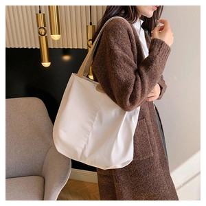 Detail of off-white canvas tote bag featuring brown woven strap and leather logo patch