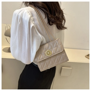 Détail d'un sac beige à surpiqûres et chaîne dorée montrant la boucle décorative ronde