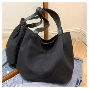 Detail of black canvas tote bag with leather straps on a blue denim jacket background