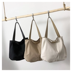 Three minimalist tote bags in black, khaki, and cream hanging on a wooden rod