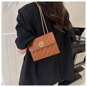 Gros plan du sac matelassé marron avec boucle dorée porté sur une veste de tailleur