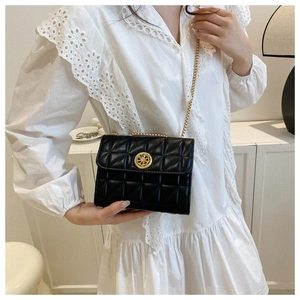 Détail d'un petit sac matelassé noir avec chaîne dorée sur une robe en dentelle