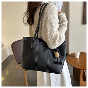 Detail of black leather tote bag with white contrast stitching and plush lamb charm