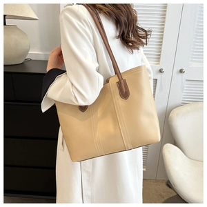 Detail showing beige and brown leather tote bag with white decorative stitching on a model