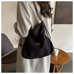 Lifestyle view of a large black canvas tote bag with brown leather straps and logo patch